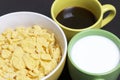 Useful breakfast. Corn sticks flakes in a container and a mug of coffee and milk. On a dark background. Royalty Free Stock Photo