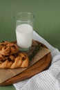 Useful breakfast on a wooden tray. Glass of milk and pastries with raisins on a green background