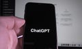 User holding SmartPhone with ChatGPT logo, and in the Background website of ChatGPT command prompt Developed by OpenAI.