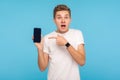 User surprised by mobile phone. Portrait of amazed shocked man in white t-shirt pointing to cellphone