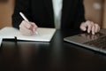 usiness woman writing marketing plan in notebook ready to use computer in office