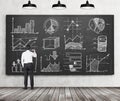 Ãâusinessman or student of finance or management programme is drawing some charts or graphs on the black chalkboard. Rear vie