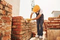 Using bricks. Young construction worker in uniform is busy at the unfinished building Royalty Free Stock Photo