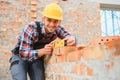 Using bricks. Young construction worker in uniform is busy at the unfinished building Royalty Free Stock Photo