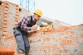 Using bricks. Young construction worker in uniform is busy at the unfinished building Royalty Free Stock Photo