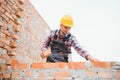 Using bricks. Young construction worker in uniform is busy at the unfinished building Royalty Free Stock Photo