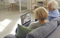 Senior couple sitting on couch with laptop and having video call with online doctor