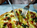 Using knife and fork to cut a pizza on a plate of fresh pizza off the oven with meat, vegetables, mushrooms, and cheese