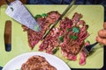 Using knife slicing beef steak on chopped board and fork stabbing beef