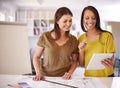 Using the latest design technology. Two female architects discussing the details of a blueprint and looking at a tablet. Royalty Free Stock Photo