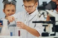 Using microscope. Children in white coats plays a scientists in lab by using equipment Royalty Free Stock Photo