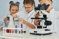 Using microscope. Children in white coats plays a scientists in lab by using equipment Royalty Free Stock Photo
