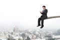 Using mobile phone businessman sitting on springboard with cityscape