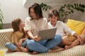 Using modern tecchnologies. Young beautiful happy caucasian family, mother and two cute little children sitting on sofa Royalty Free Stock Photo