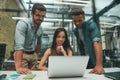 Using modern technologies. Group of three young and cheerful employees looking at screen of laptop and smiling while Royalty Free Stock Photo