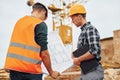 Using paper document with plan on it. Two construction workers in uniform and safety equipment have job on building together Royalty Free Stock Photo