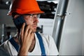 Using phone. Portrait of engineer in metallurgical factory in protective helmet and eyewear