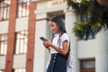 Using smartphone. School girl in uniform is outdoors near the building