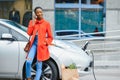 Using smartphone while waiting. African American girl on the electric cars charge station at daytime. Brand new vehicle