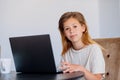 Smiling little Caucasian girl having video call in remote classroom with teacher using laptop, happy little kid greeting with tuto