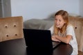 Smiling little Caucasian girl having video call in remote classroom with teacher using laptop, happy little kid greeting with tuto