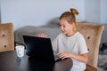 Smiling little Caucasian girl having video call in remote classroom with teacher using laptop, happy little kid greeting with tuto