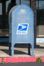 USPS blue outdoor mailbox. Weathered mail collection box of United States Postal Service standing next to the red fire lane. - San