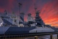 The USS North Carolina With Guns And People Walking On The Deck Of The Ship And Powerful Clouds At Sunset