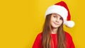 ÃÂ¡ute little girl wearing Christmas Santa hat standing isolated over yellow background, looking at camera
