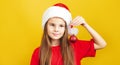 ÃÂ¡ute little girl wearing Christmas Santa hat standing isolated over yellow background, looking at camera