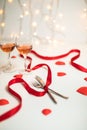 Valentine`s day display of a dinner preparation with cutlery, red ribbon, glasses of wine and heart symbols Royalty Free Stock Photo