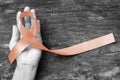 Uterine and Gynecologic Cancer Awareness peach color ribbon on womanÃ¢â¬â¢s hand support and aged wood isolated with clipping path