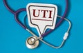 UTI - acronym on white figure sheet on a blue background with a stethoscope