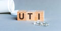 UTI - acronym from wooden blocks with letters, abbreviation UTI urinary tract infection, concept, grey background with ampoules