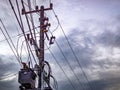 Utility pole infrastructure with transformer and tangled overhead electrical wires against cloudy sky Royalty Free Stock Photo