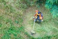 Maintenance of the green lawn of the city park. A man mows the grass with a petrol trimmer, top view Royalty Free Stock Photo