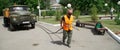 A utility worker wearing a protective antivirus mask drags a large tank car through a city park by a hose. Funny case. June 2,