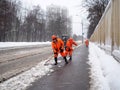 Utility workers in orange uniforms shovel muddy wet snow from the sidewalk