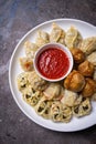 Uzbek samsas and manti with meat, pumpkin and greens on a plate with red sauce