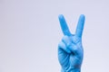 V sign is showed by right man hand in a blue medical glove on a white background. The symbol of Victory