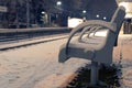 Vacant bench covered with snow at an empty train station at night