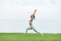 Vacation of Attractive Asian woman relaxing in yoga Warrior one pose on green grass and beach with sunset beautiful sea Royalty Free Stock Photo