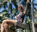 Vacation concept. Happy young woman in white dress and hat swinging at palm grove. Royalty Free Stock Photo