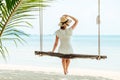Young woman in white dress and hat swinging at a beach Royalty Free Stock Photo