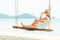 Young woman in white dress and hat swinging at a beach Royalty Free Stock Photo