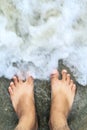 Vacation on the ocean beach, feet on the sea sand. Standing on the beach with ocean waves cover the leg, looking from top.