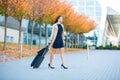 Vacation. Smiling female passenger proceeding to exit gate pulling suitcase through airport concourse