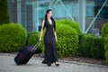 Vacation. Smiling female passenger proceeding to exit gate pulling suitcase through airport concourse Royalty Free Stock Photo