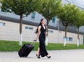 Vacation. Smiling female passenger proceeding to exit gate pulling suitcase through airport concourse Royalty Free Stock Photo