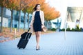 Vacation. Smiling female passenger proceeding to exit gate pulling suitcase through airport concourse